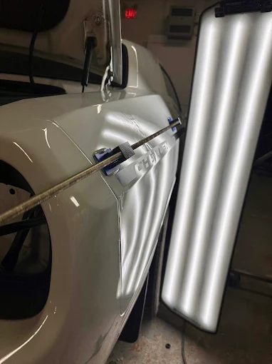 Close-up of a dent being worked out of a panel with paintless dent repair tools