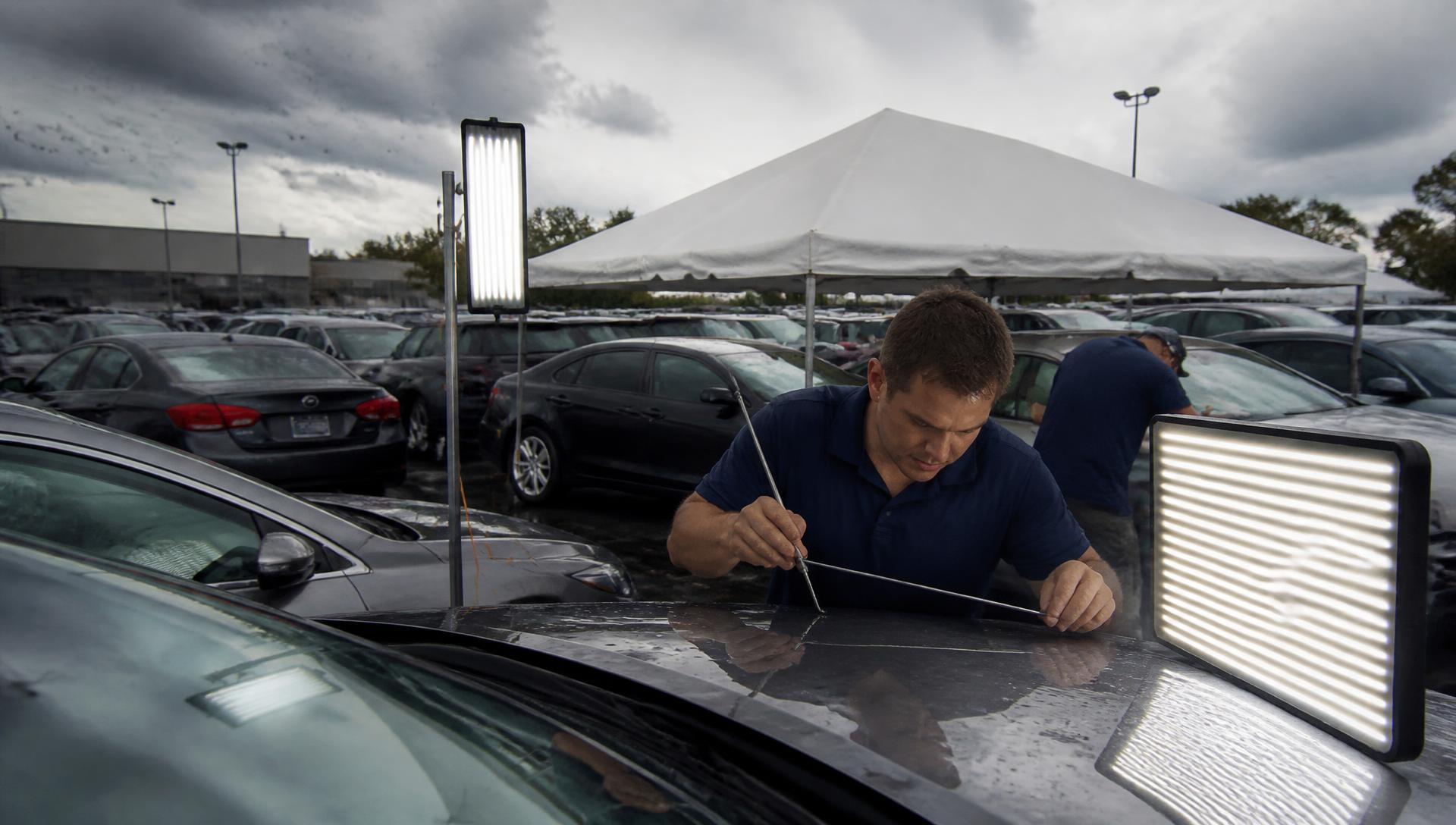 Precision Dent Repair hail catastrophe crew working hail-damaged dealership inventory on site under portable PDR lighting and a temporary work tent